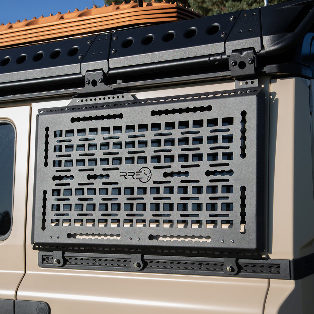 A Black Exterior cargo carrier made by Rough Road Equipment with the RRE logo stamped into it, shown on an Ineos Grenadier. Featuring three different attachment points for various systems like L-track (Airline Track), MOLLE, and Carrage bolt. Show with the optional LeTech roof rack attachment mount and the LeTech roof rack. MaxTraxx not included. 